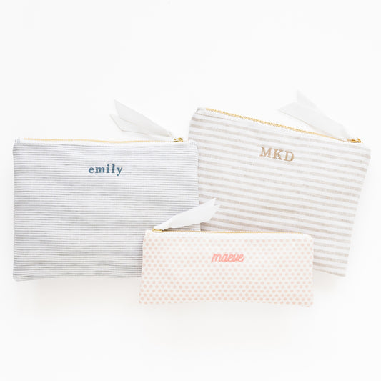 Striped and dot fabric pouches in various colors and sizes with names embroidered on them
