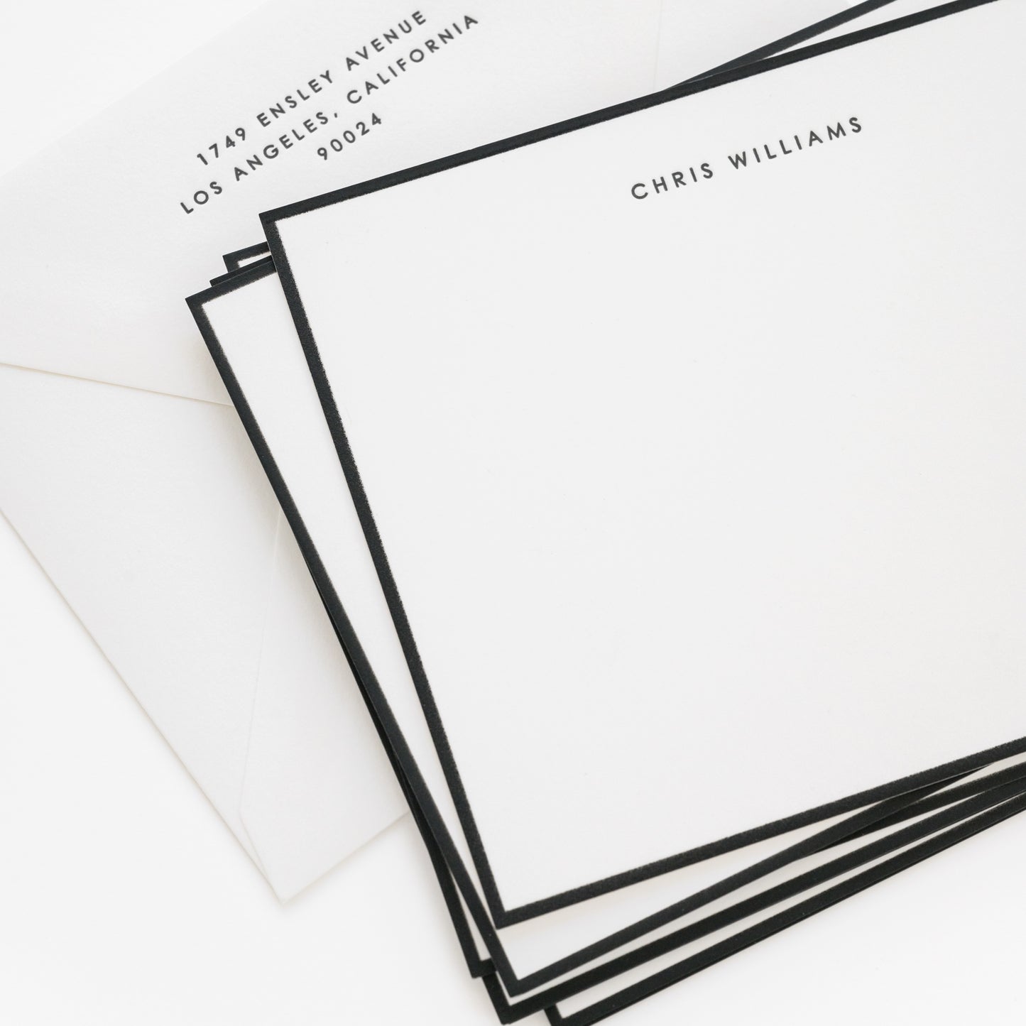 Stack of black bordered flat stationery cards with 'chris williams' and address on the envelope