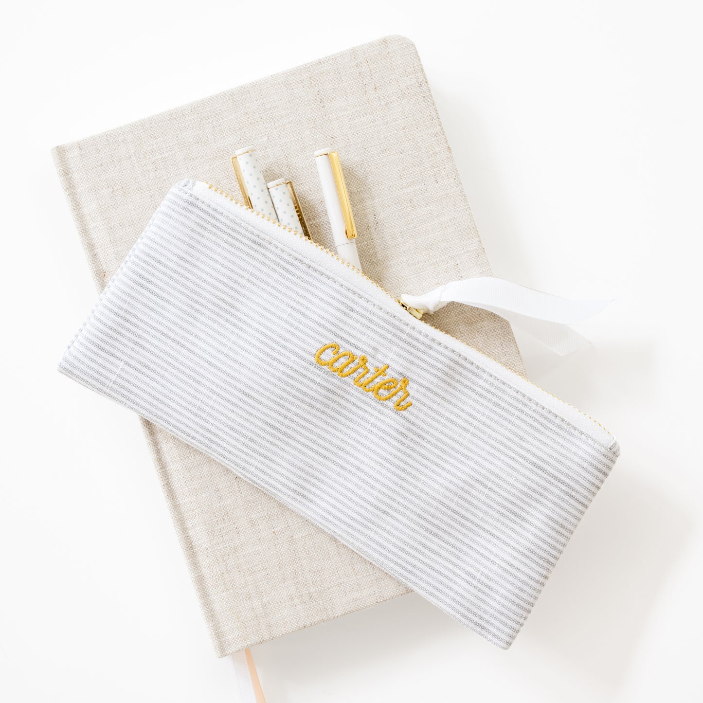 White stripe pouch with 'carter' embroidery on a beige fabric journal with pens inside