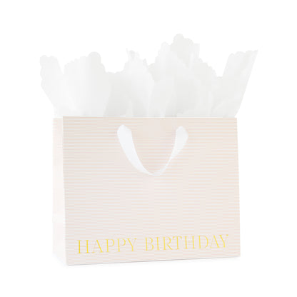 large gift bag with white ribbon handles with a pink stripe pattern printed with happy birthday in gold foil with white scallop tissue paper