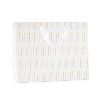 large gift bag with white ribbon handles printed with a colorful candle pattern in pink and blue with gold foil