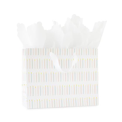 large gift bag with white ribbon handles printed with a colorful candle pattern in pink and blue with gold foil with white scallop tissue paper