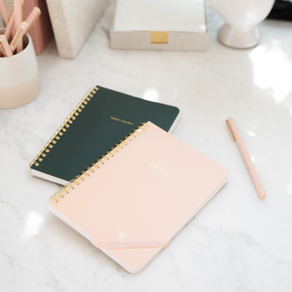 Green Habit Tracker and Pink Goal Tracker Spiral Notebooks on a counter with a pink pen