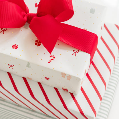 Stack of multiple holiday wrapped gifts with red stripe wrap, green stripe, and a multicolor holiday icon wrap tied with a big red bow