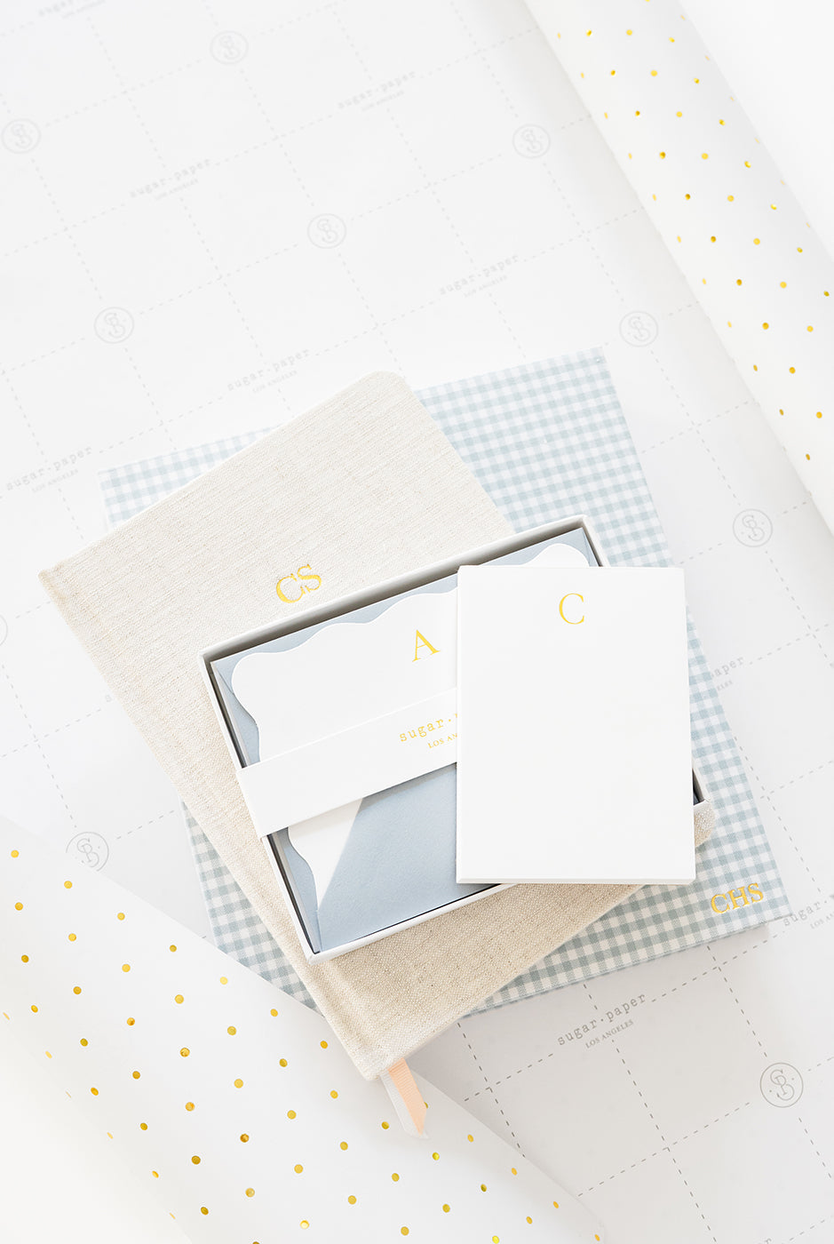 A notepad, note set, journal, and fabric-bound keepsake book with gold monograms on gift wrap.