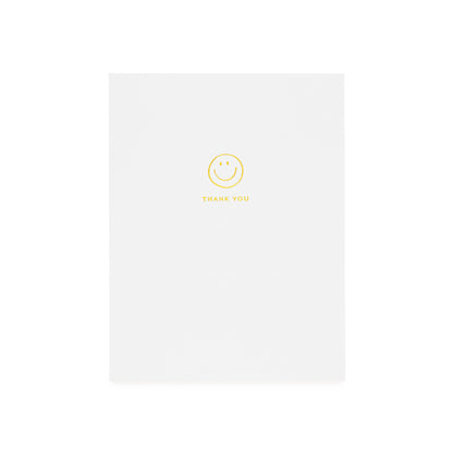 White greeting card printed with gold foil smiley icon and 'thank you'