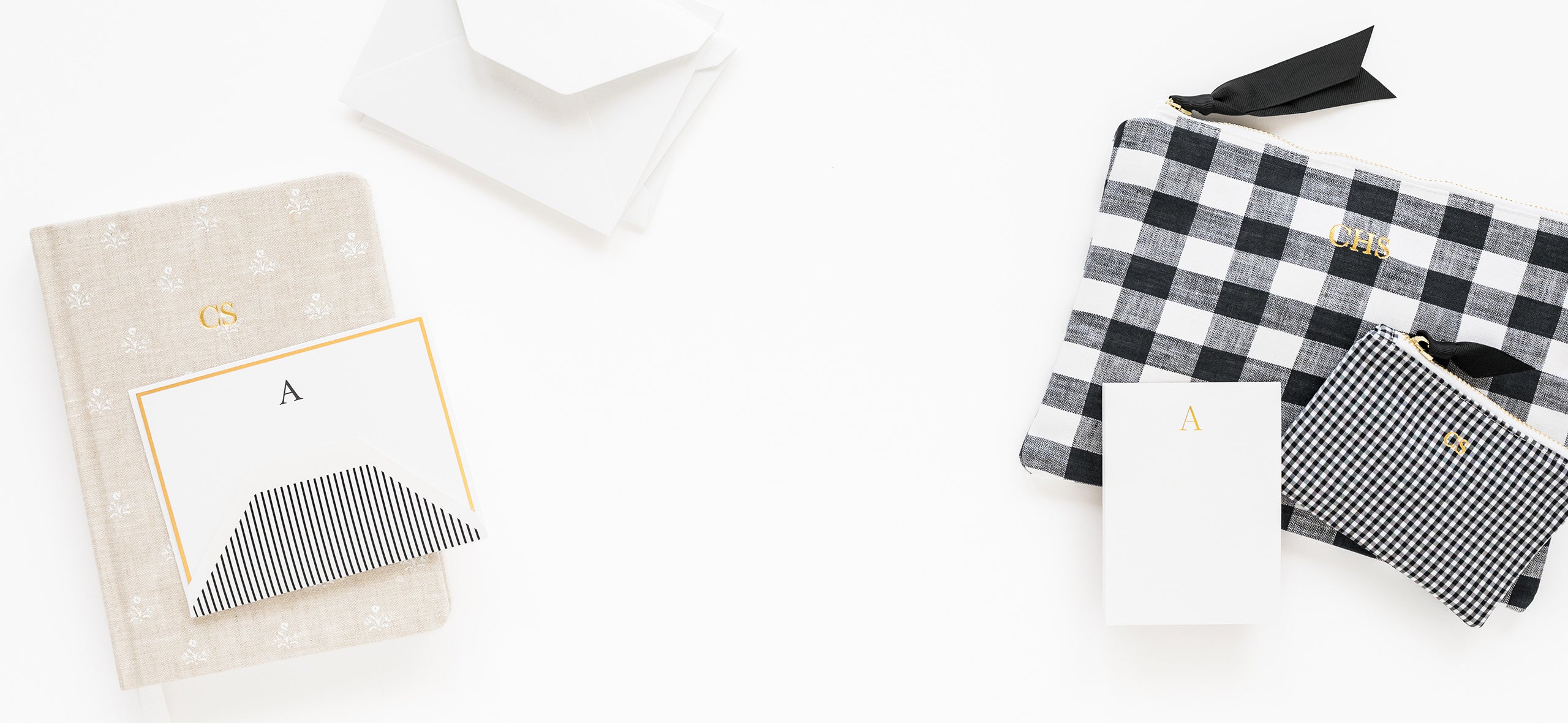 Black and white checkered pouches with gold foil stamped initials and a flax floral fabric journal with gold foil "cs" initials, white "a" notepad and "a" monogram note set