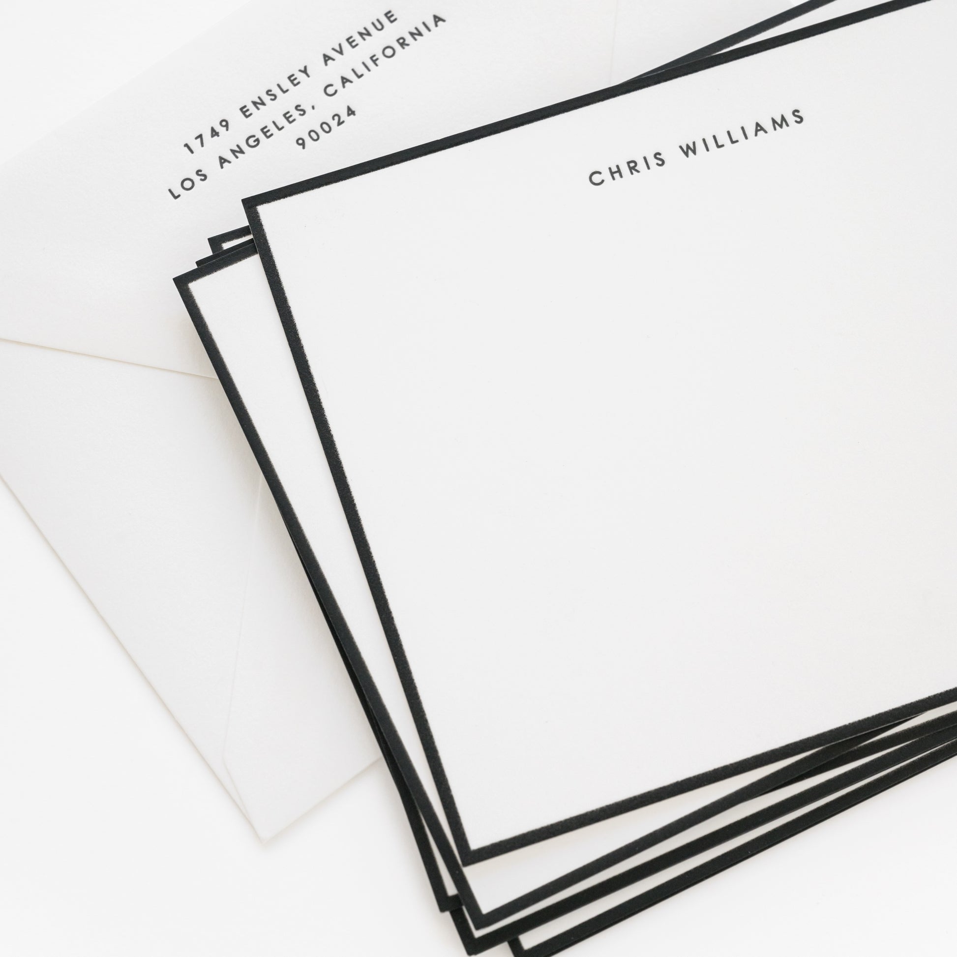 Stack of black bordered flat stationery cards with 'chris williams' and address on the envelope
