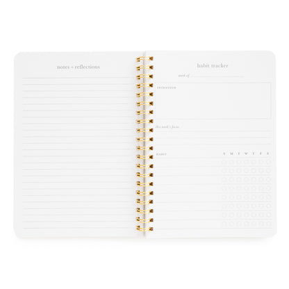 Interior of habit tracker spiral notebook with "notes and reflections" page and "habit tracker" goals with space for "intention," "this week's focus" and space to write habit and mark off for each day of the week
