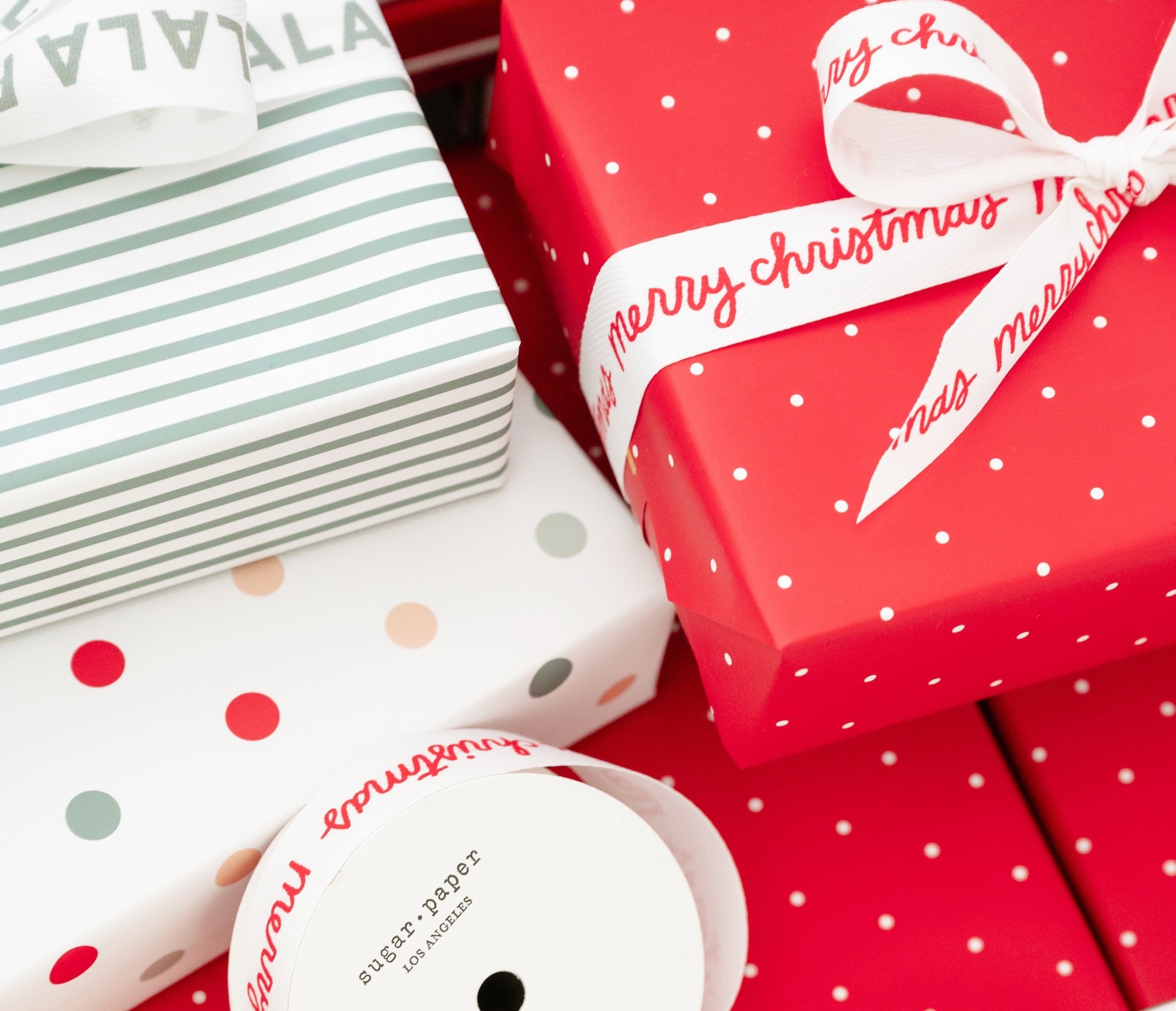Close-up of Christmas gift wrap with red box, striped paper, and polka dot patterns with message ribbon printed with "merry christmas" in red on white ribbon and "falalala" printed in green on white ribbon