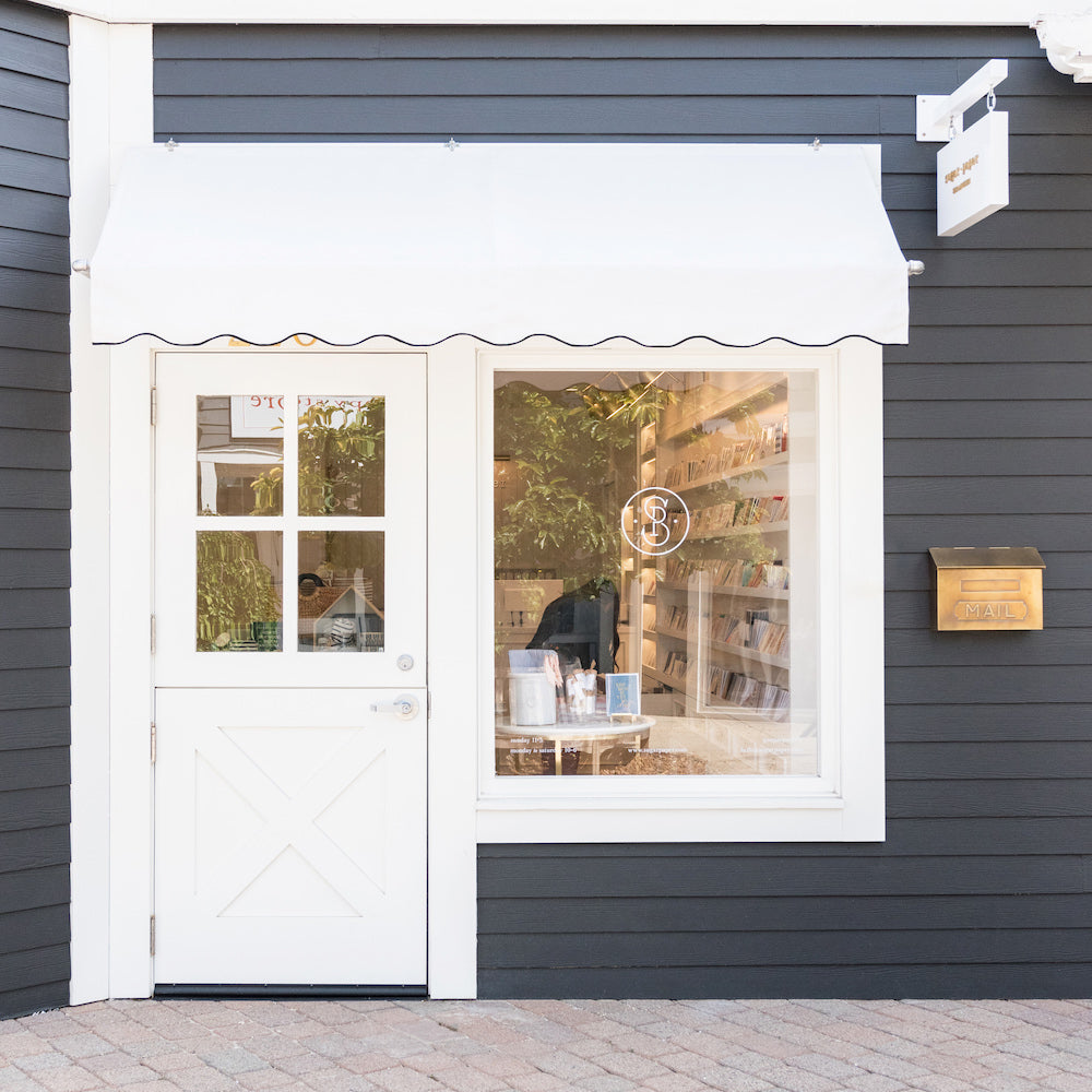 Storefront of sugar paper store with white awning and gold mailbox
