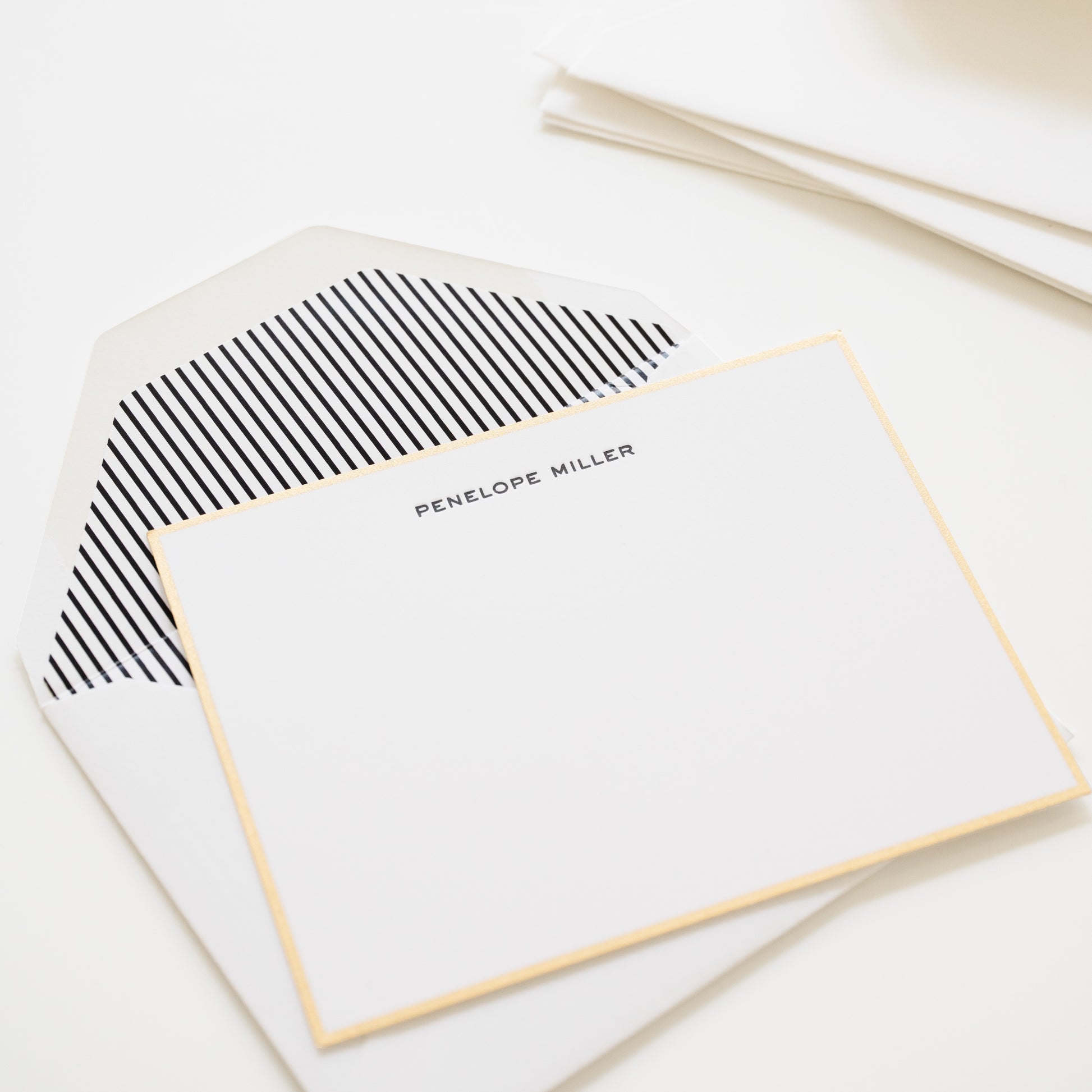 Gold bordered card with 'penelope miller' in black ink and black stripe envelope liner