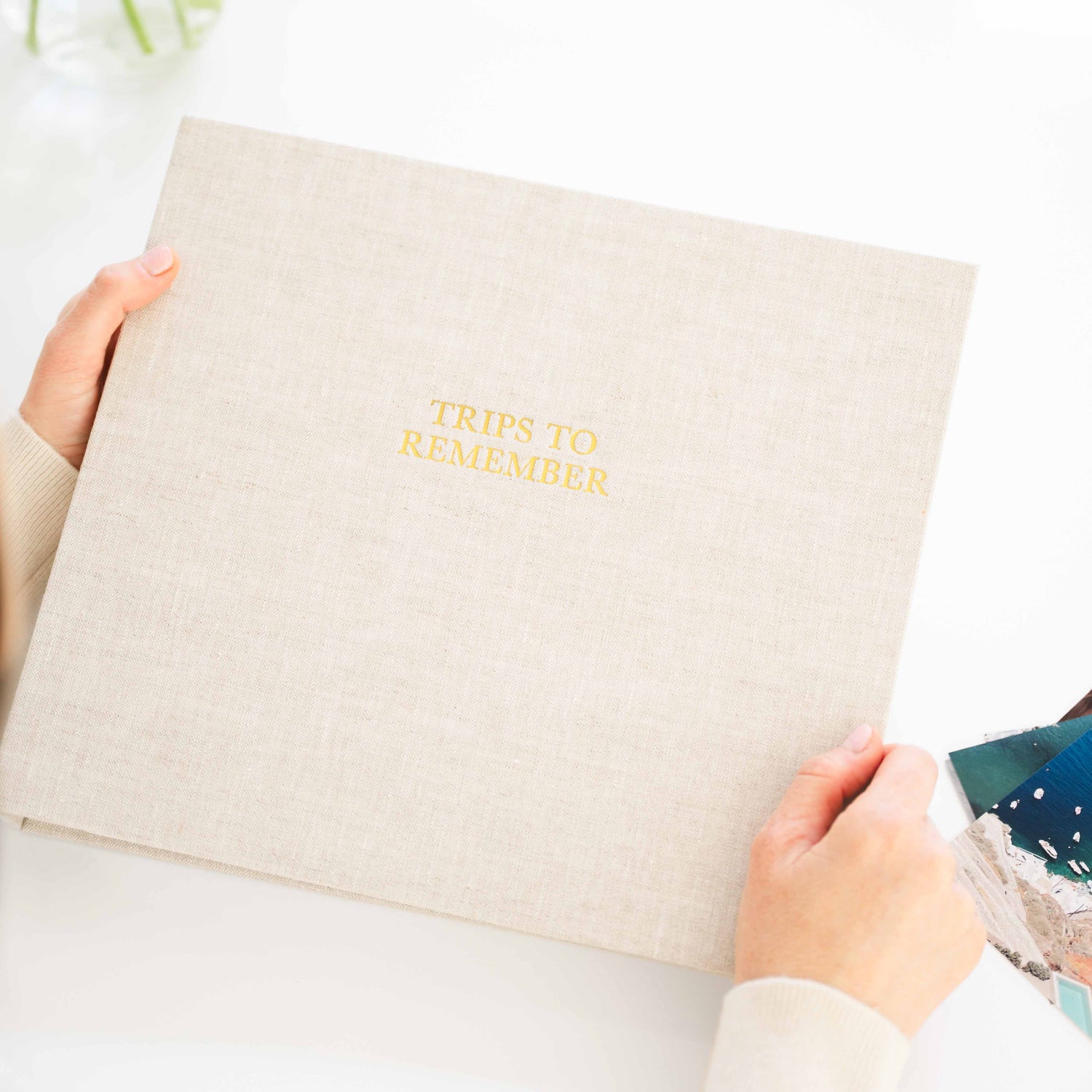 A person holds a flax linen photo album with gold foil text reading 'TRIPS TO REMEMBER'