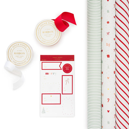 Photo of multiple rolls of wrapping paper in a white and red diagonal stripe, multicolor holiday icon wrap, and green stripe wrap patterns with two ribbon rolls in white and red and christmas stickers