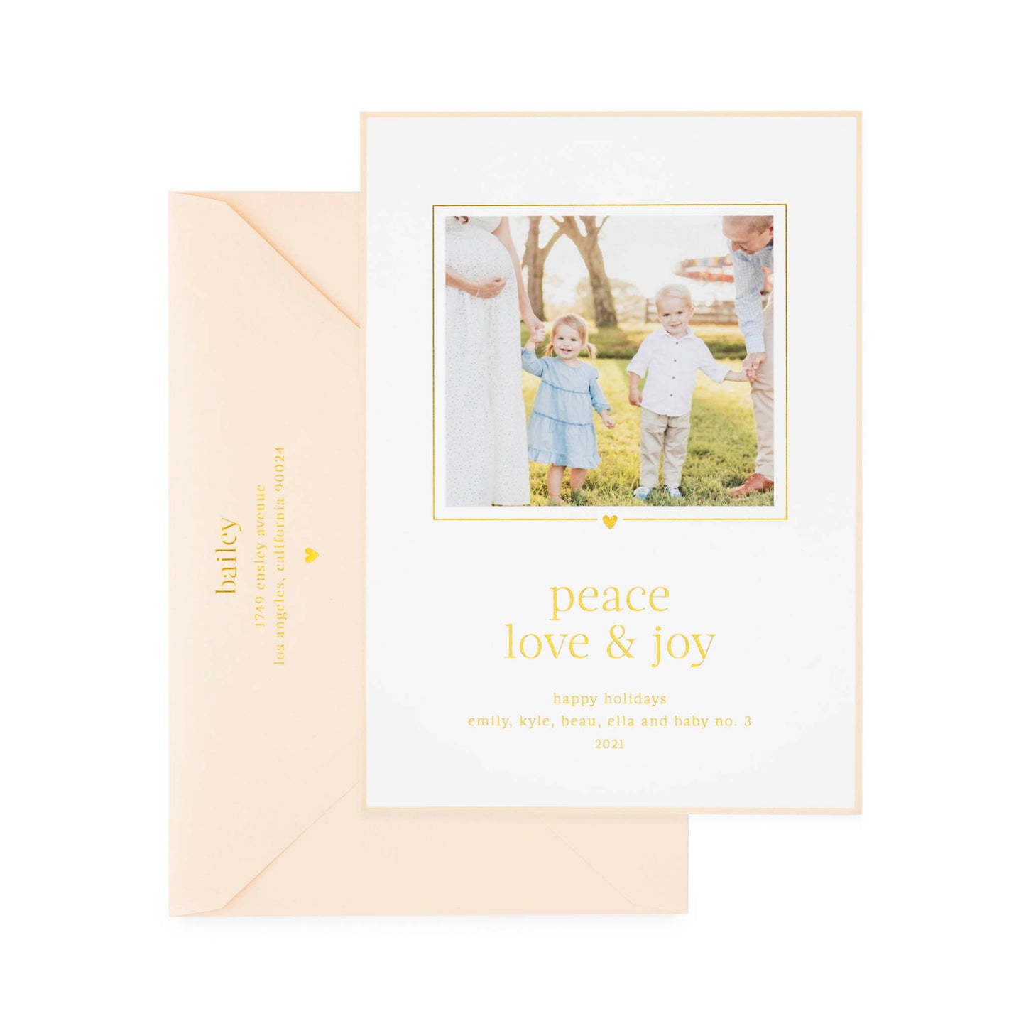 White custom holiday photo card printed with "peace love and joy" in gold foil with a photo of two kids and parents with a pink card border paired with a pink envelope
